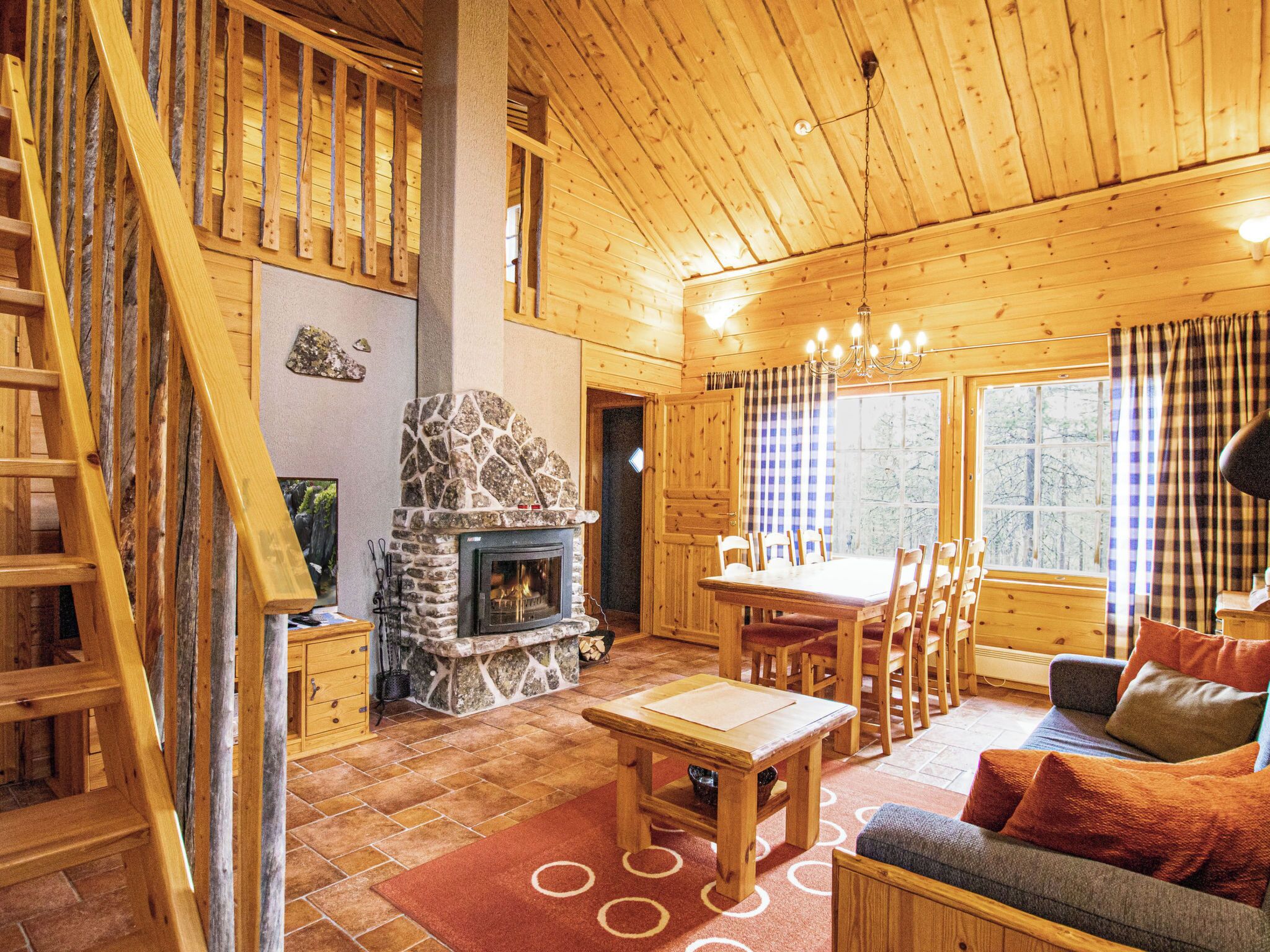 A wooden cabin interior with a stone fireplace, a dining area, and a sofa.