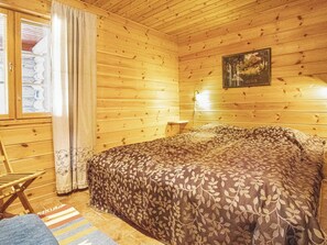 Een houten kamer met een bed, een klein tafeltje en een raam met gordijnen.
