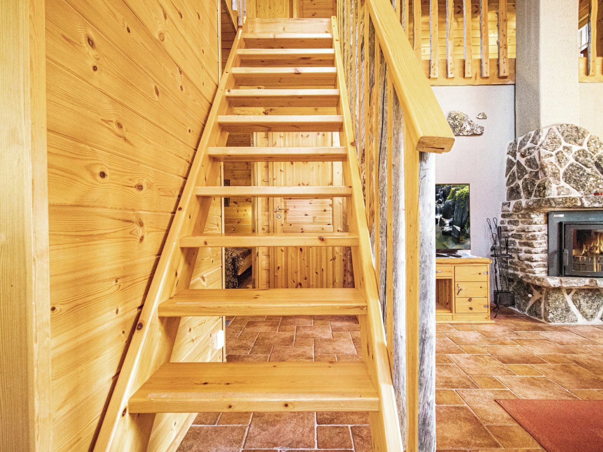 A wooden staircase leading to a stone fireplace with a tiled floor.