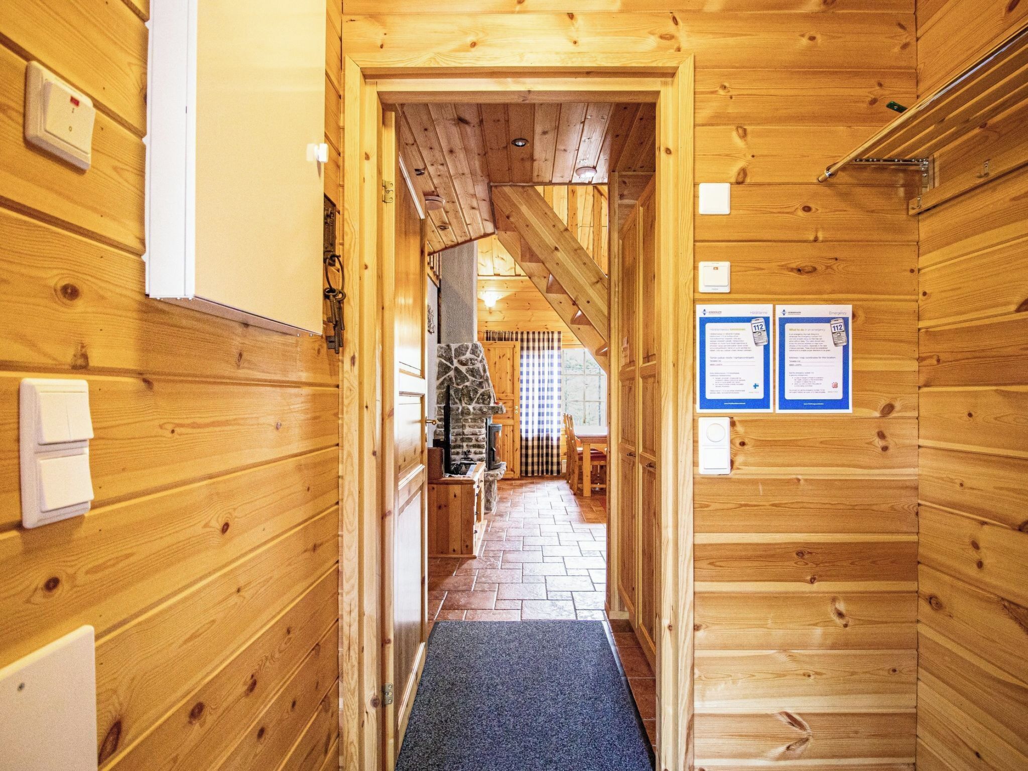 A wooden interior hallway with a stone fireplace, wooden walls, and emergency contact information on the wall.