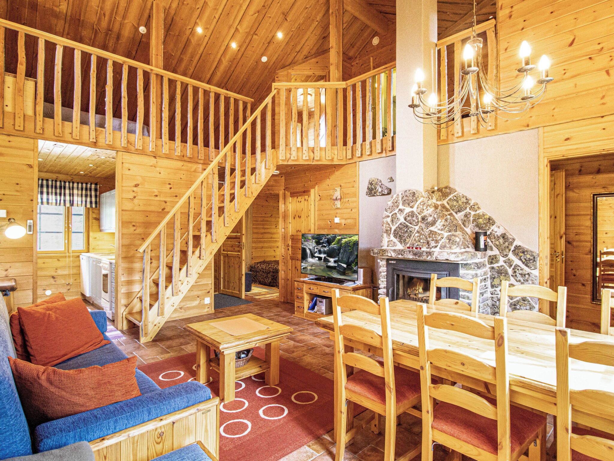 Interior de madera con escalera, chimenea, televisor y comedor.