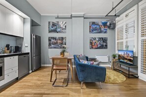 A modern kitchen with a built-in refrigerator, a dining area with a blue sofa and a table, and a living space with a TV and artwork on the walls. - Temple Court Suite in Melbourne CBD (Melbourne)