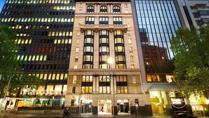 Un edificio de varios pisos con un estilo arquitectónico clásico, que presenta una entrada central con un amplio frente de vidrio.