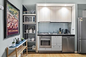 A compact kitchen with white cabinets, a stainless steel refrigerator, a built-in oven, and a microwave. - Temple Court Suite in Melbourne CBD (Melbourne)