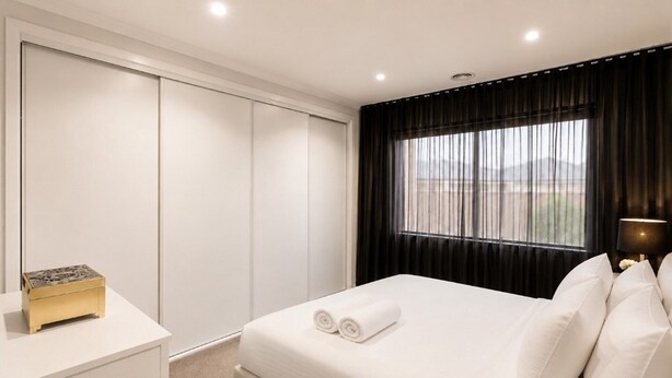 A hotel room with a bed, a bedside table, a lamp, and a window with curtains. - Spacious 4-Bedroom Family Home in Manor Lakes (Manor Lakes)