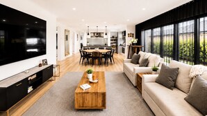 A modern living room with a TV, sofa, coffee table, and dining area. - Spacious 4-Bedroom Family Home in Manor Lakes (Manor Lakes)