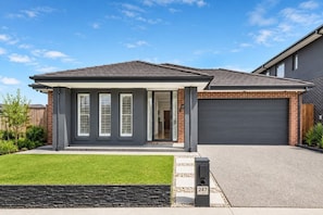 Ein modernes, zweistöckiges Haus mit überdachter Veranda, Garage und gepflegtem Rasen.