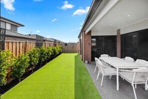 A modern outdoor patio with a dining table and chairs, a well-maintained lawn, and a wooden fence. - Spacious 4-Bedroom Family Home in Manor Lakes (Manor Lakes)