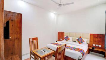 A hotel room with a bed, two chairs, a small table, a nightstand, and a ceiling fan.