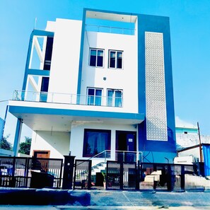 A modern two-story building with a balcony on the upper floor, a gated entrance, and a vertical decorative panel on the side. - Hotel AVS Grand (Lucknow)