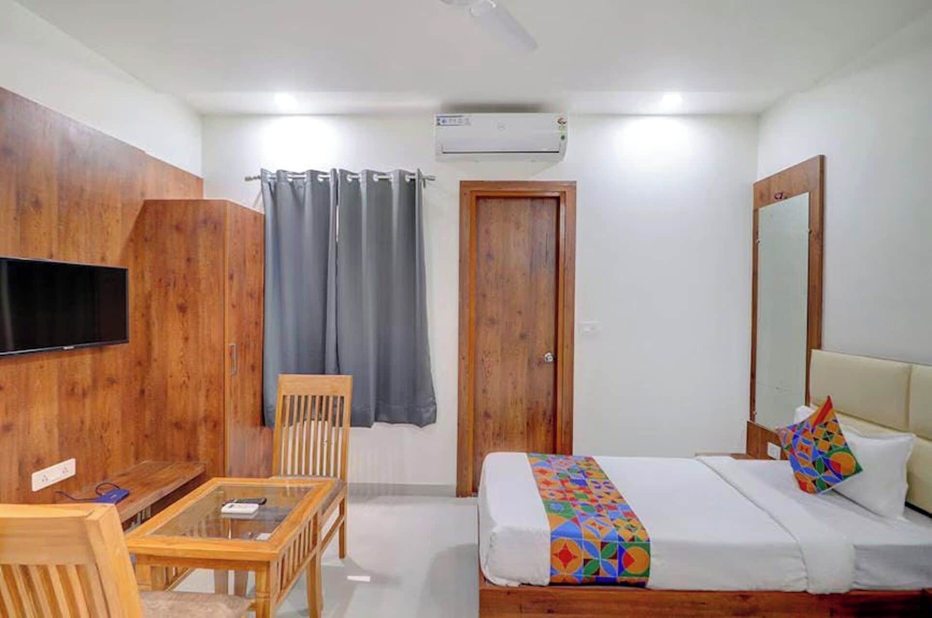 Habitación de hotel con cama, escritorio, silla, televisor, armario, espejo y aire acondicionado.