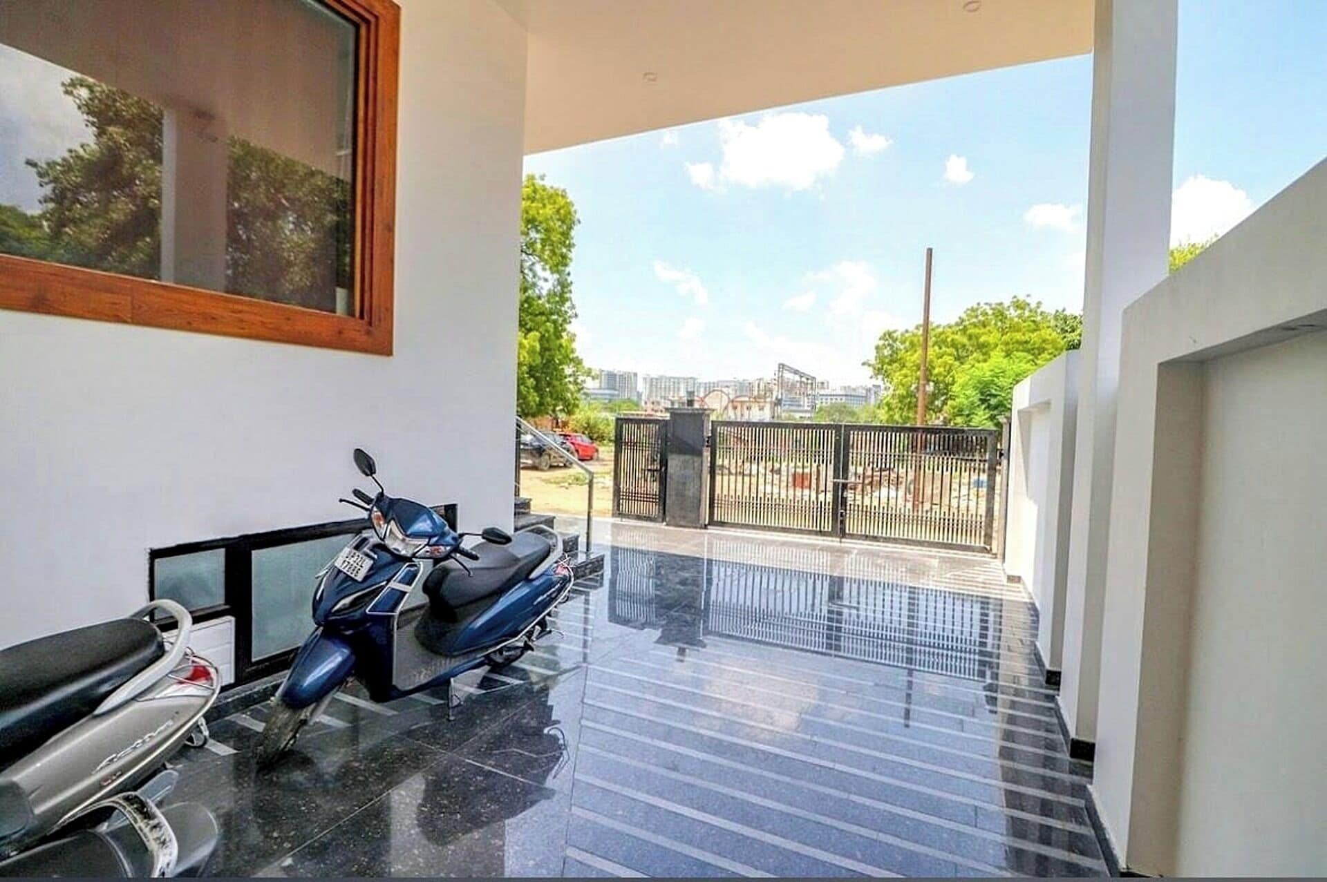 Un espacio interior moderno con una moto estacionada cerca de una ventana, una escalera que conduce a un área exterior y vistas de un paisaje urbano.