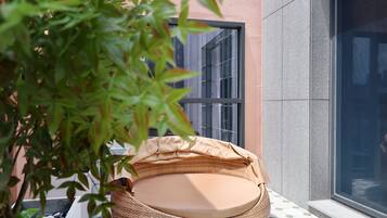 A wicker chair with a cushion, positioned on a tiled floor, adjacent to a building with a large window.