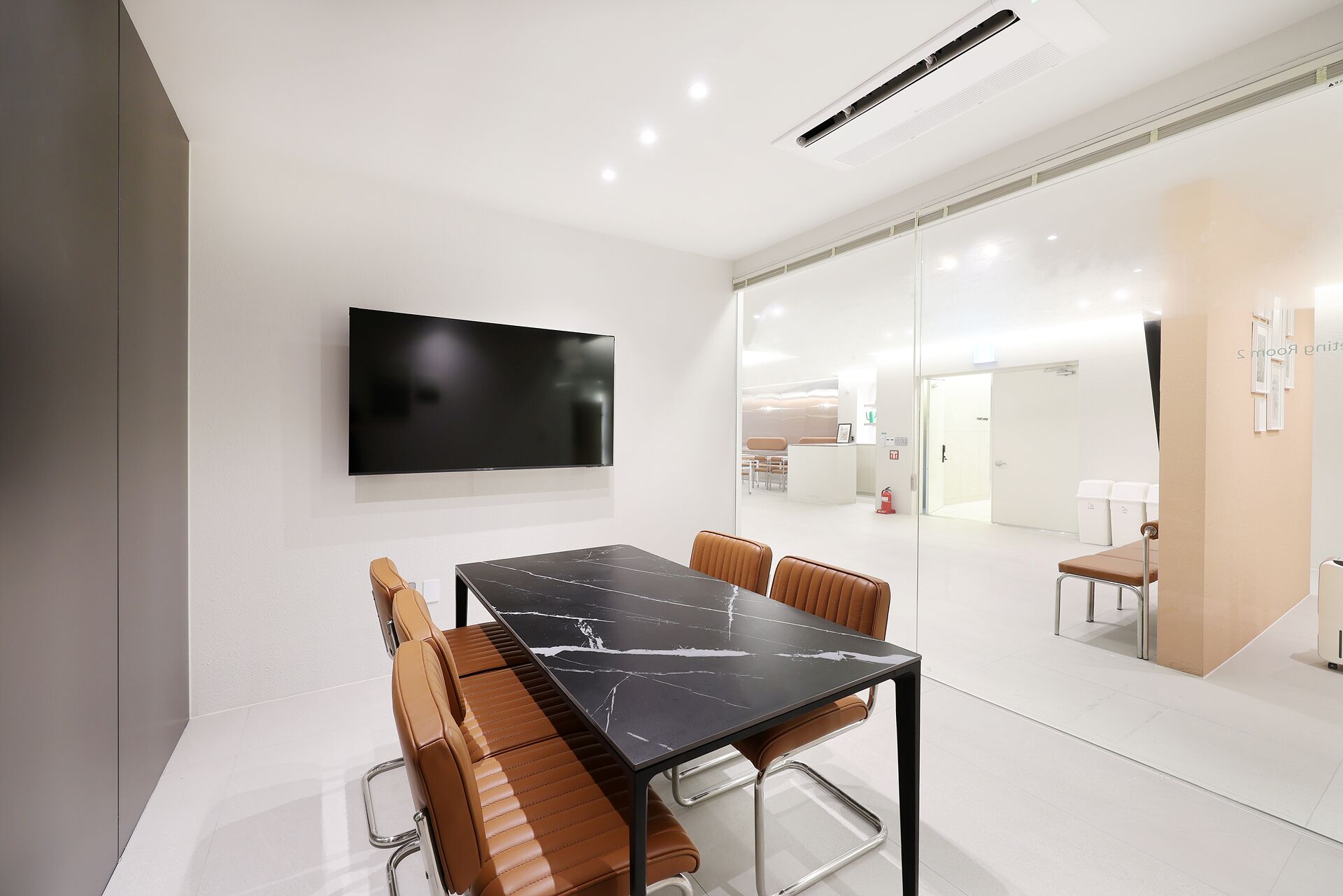 A modern conference room with a large flat-screen TV, a marble table, and leather chairs.