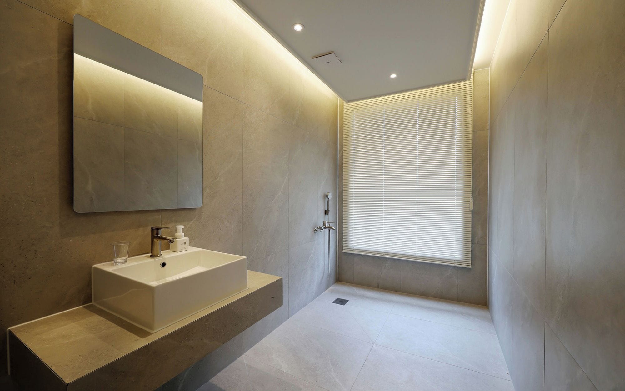 Un baño moderno con un espejo grande, un lavamanos blanco y una zona de ducha.