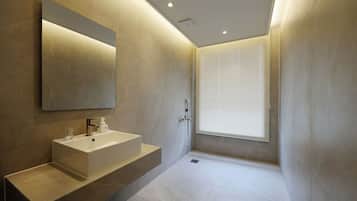 Un baño moderno con un espejo grande, un lavamanos blanco y una zona de ducha.
