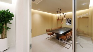 A meeting room with a long table, chairs, a potted plant, and a ceiling vent.