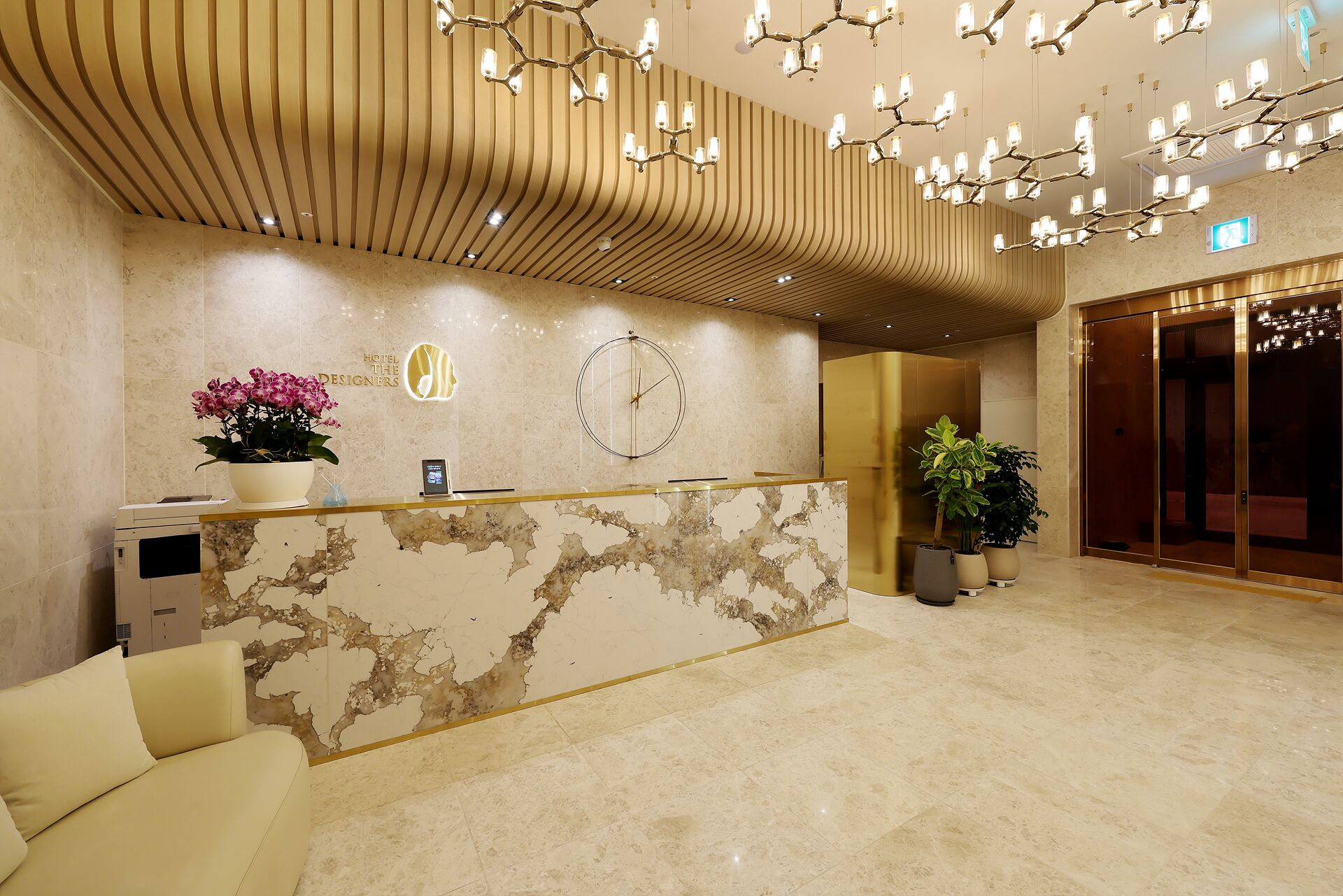 Zona de recepción de un hotel con mostrador de mármol, un reloj y un escritorio.