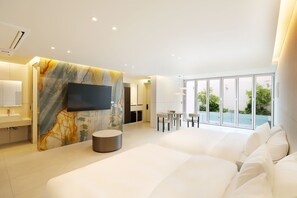 Habitación de hotel moderna con una cama grande, un televisor de pantalla plana montado en una pared de mármol, una mesita redonda con sillas y un balcón con vistas a zonas verdes.