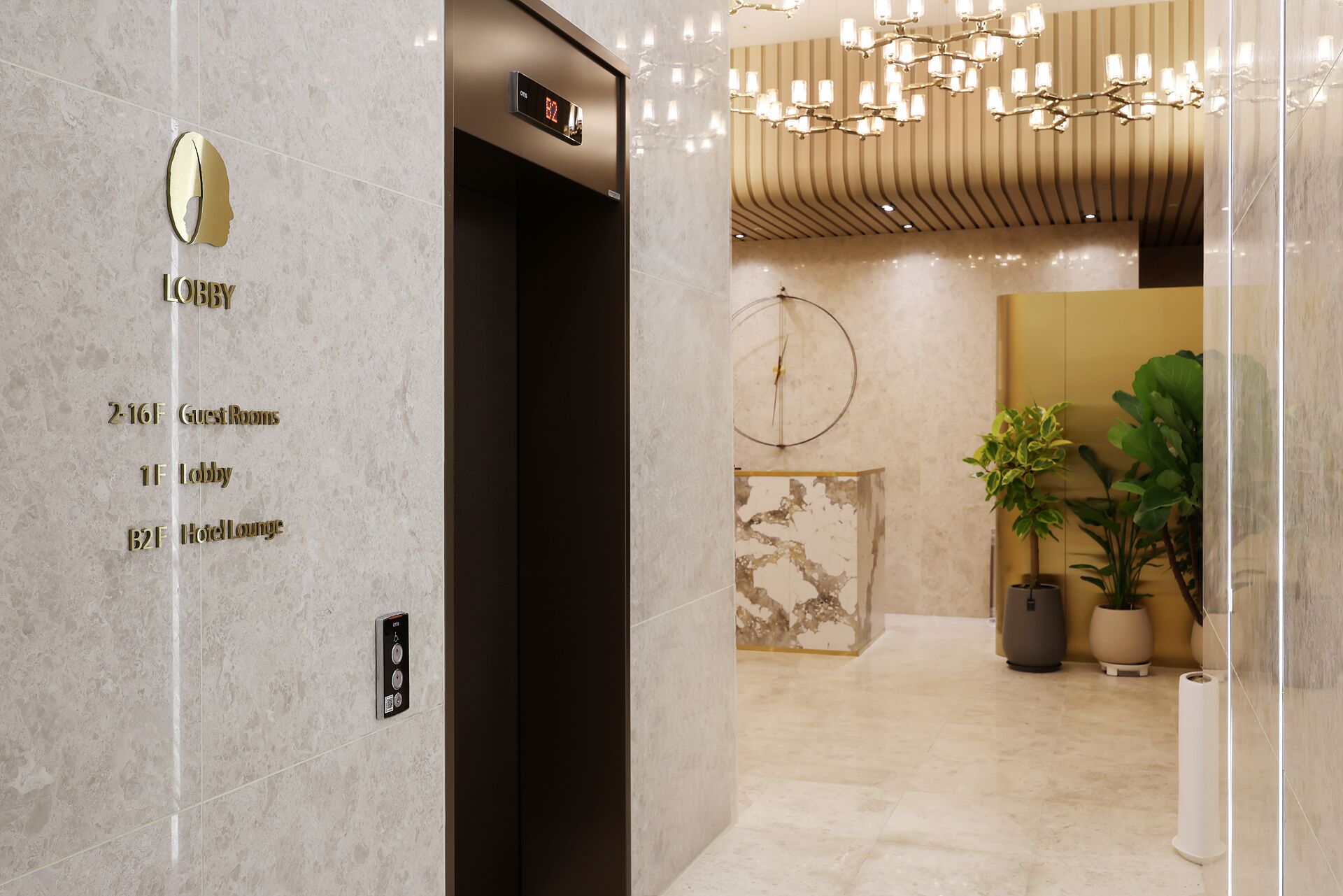A hotel lobby with a marble floor, a reception desk, and a wall-mounted elevator with a digital display.