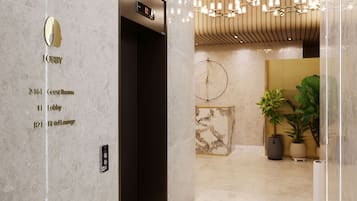 A hotel lobby with a marble floor, a reception desk, and a wall-mounted elevator with a digital display.