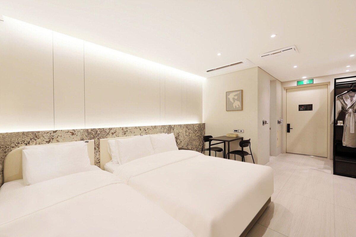 A hotel room with a large bed, a small table, and a wardrobe.
