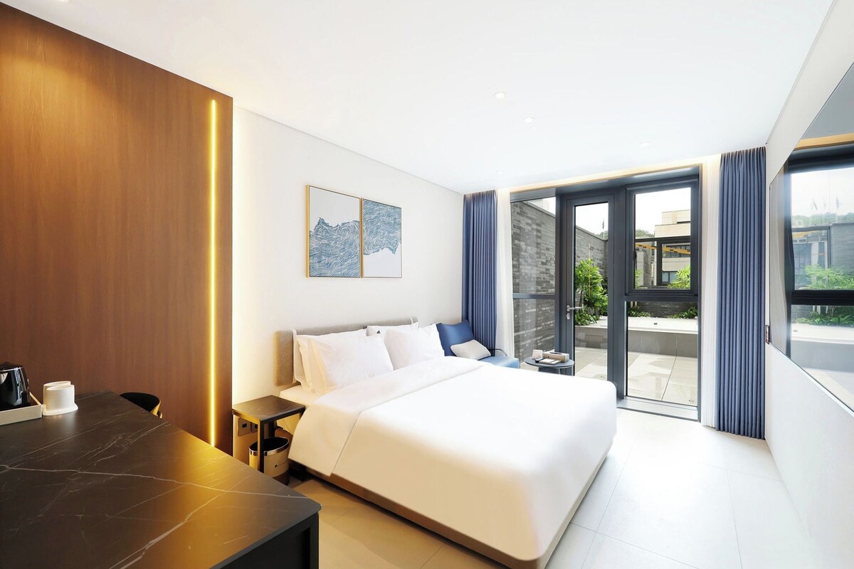 A modern hotel room with a large bed, a desk, and a view of the outside.