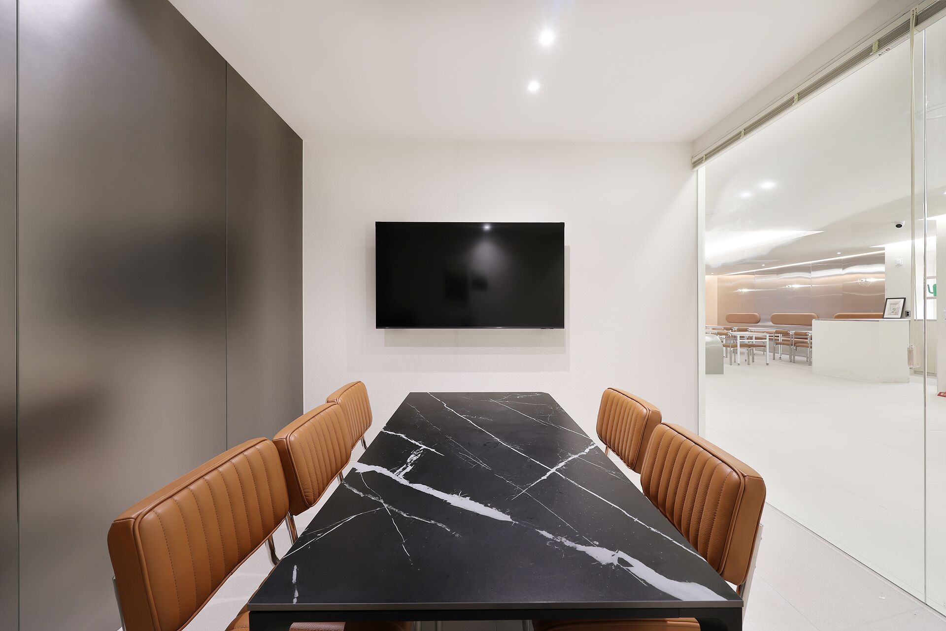 A conference room with a black marble table, leather chairs, a flat-screen TV, and a glass partition.