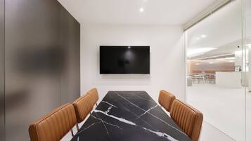 A conference room with a black marble table, leather chairs, a flat-screen TV, and a glass partition.