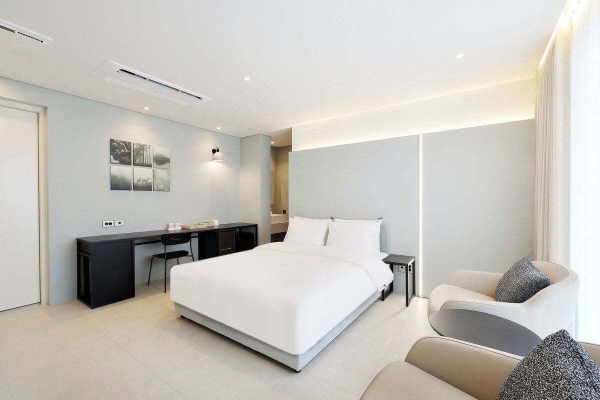 A modern hotel room with a large bed, a desk, and a seating area.