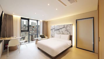 A hotel room with a bed, a desk, a chair, and a view of the city.