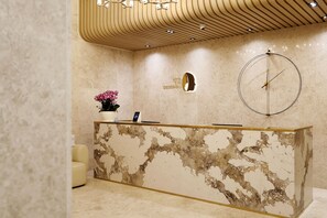 A hotel reception desk with a marble design, a clock, and a potted plant.