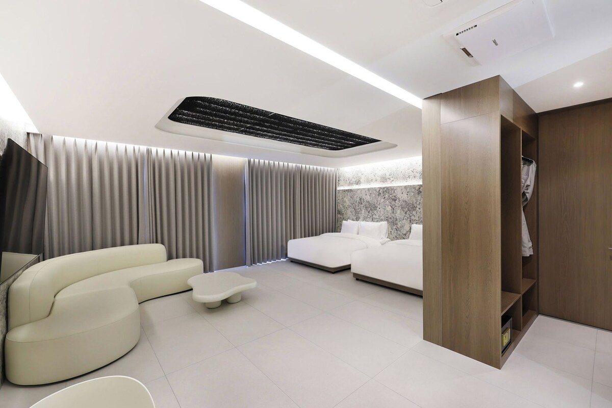 A modern bedroom with a bed, a seating area with a sofa and a small table, and a wardrobe.