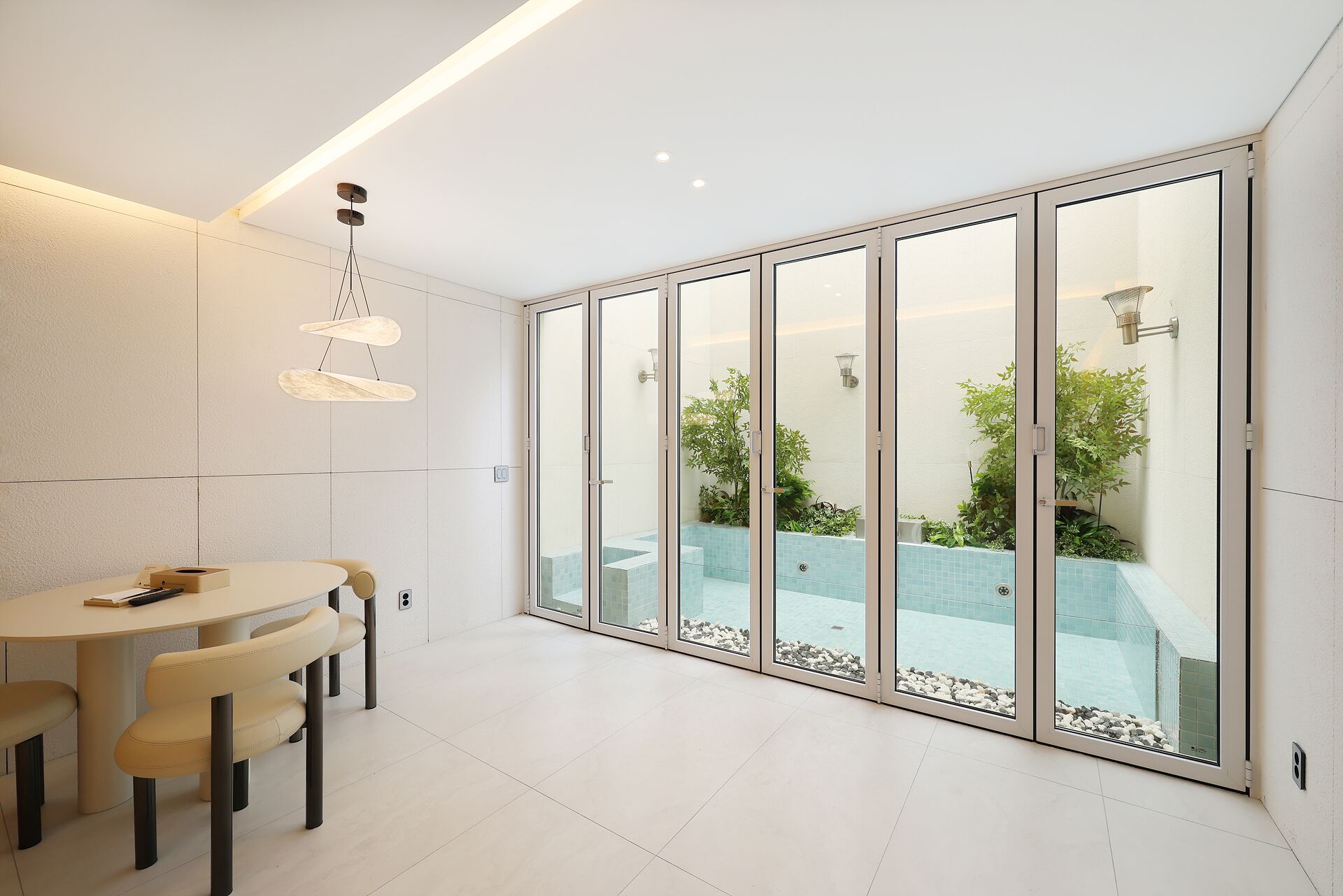 A modern interior with a dining area, a glass-enclosed balcony with a pool, and recessed ceiling lighting.