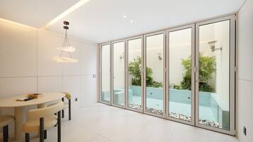 A modern interior with a dining area, a glass-enclosed balcony with a pool, and recessed ceiling lighting.