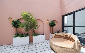 A balcony with a wicker sofa, potted plants, and a view of the city.