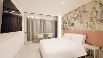 A modern hotel room with a bed, bedside table, and a seating area with a table and chairs.