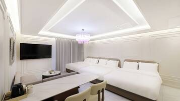 Une chambre d’hôtel moderne dotée d’un grand lit, d’un téléviseur à écran plat fixé au mur, d’un coin repas avec une table et des chaises, et d’un lustre.