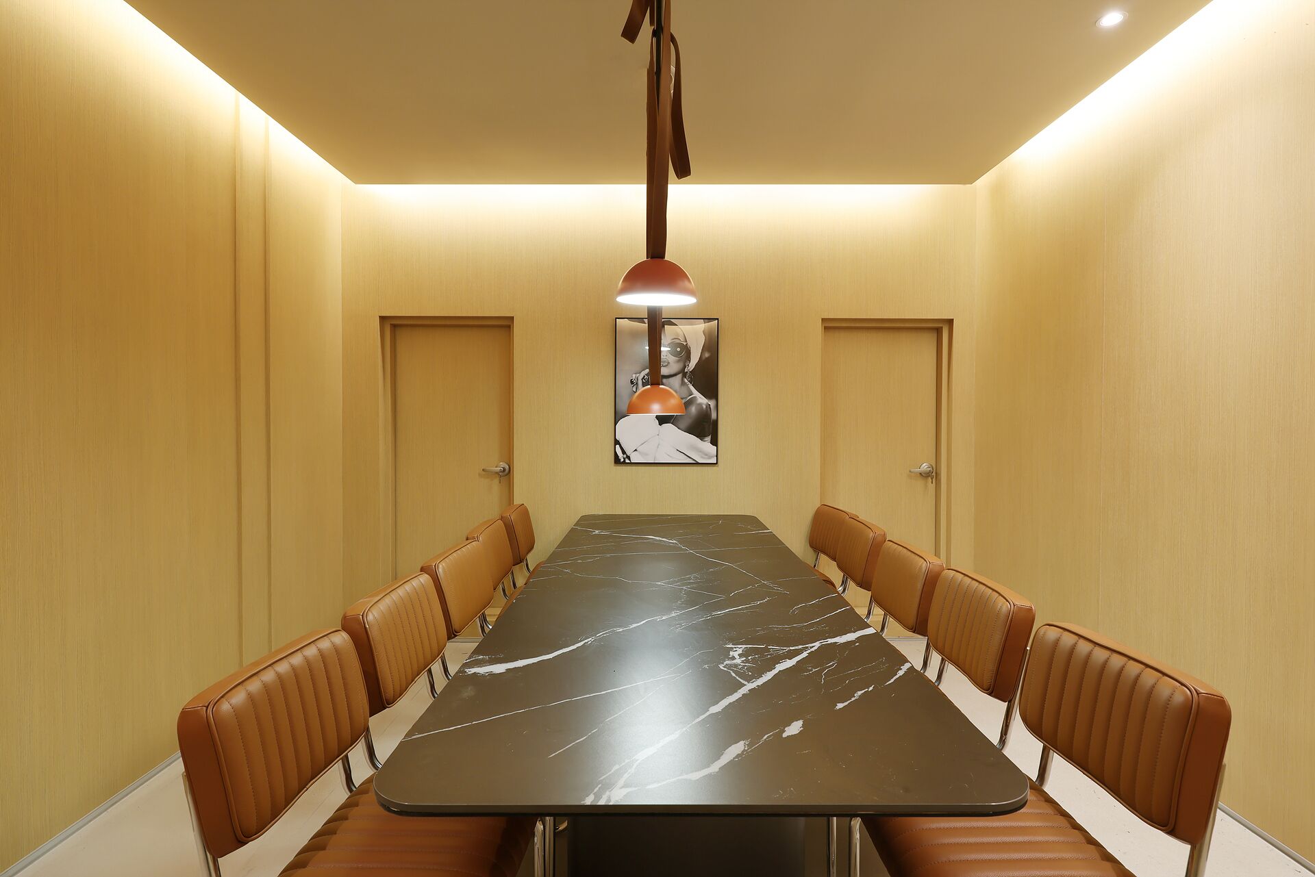 A conference room with a long table and leather chairs, a pendant light, and a framed picture on the wall.