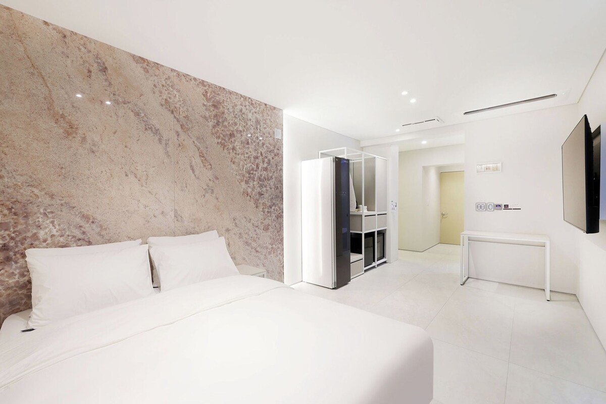 A modern hotel room with a large bed, a marble accent wall, a wardrobe, and a television.