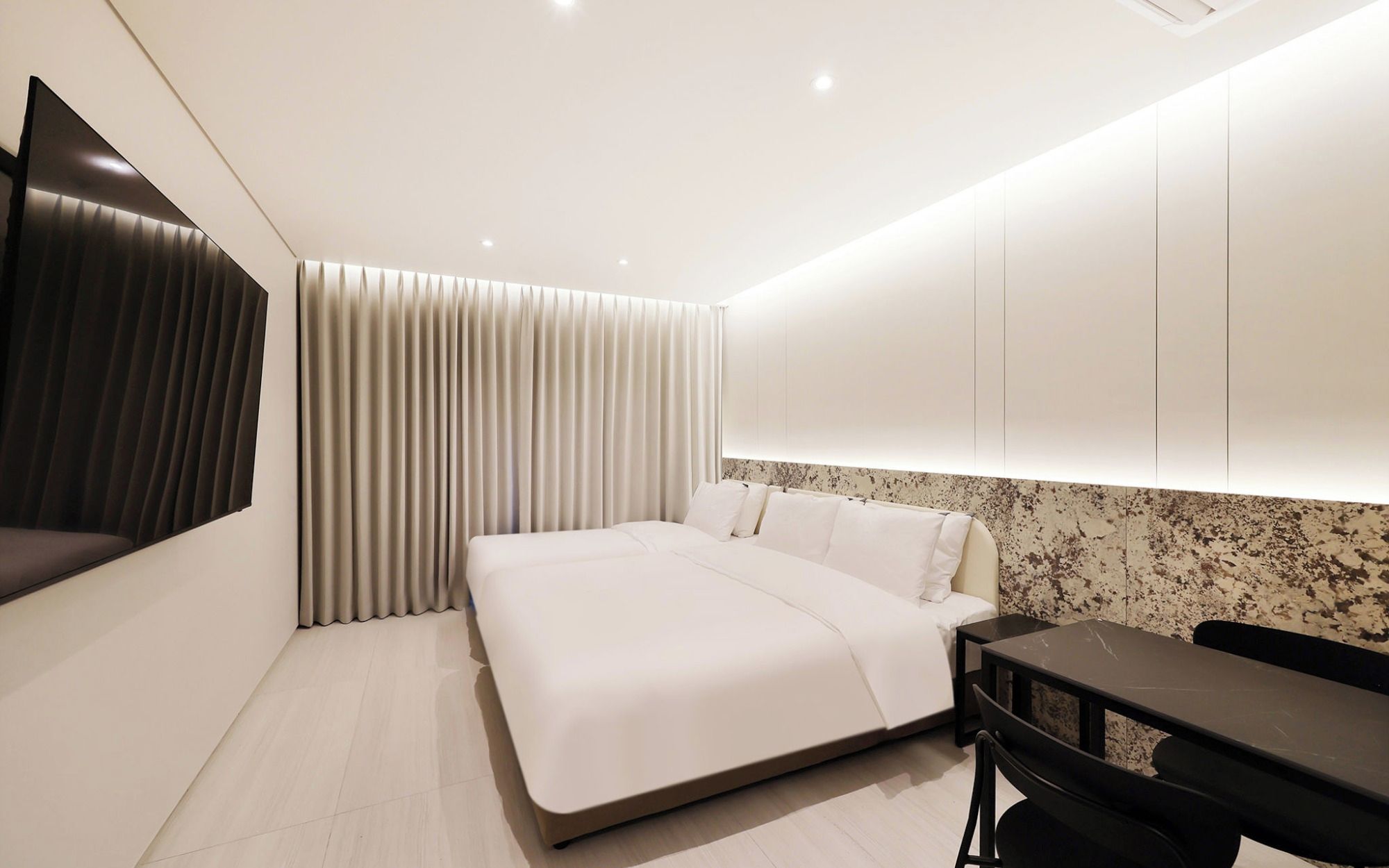 A modern hotel room with a bed, a desk, and a large window with curtains.