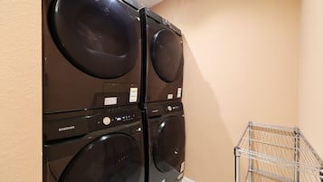 A laundry area with stacked washers and dryers, a metal drying rack, and a beige wall.