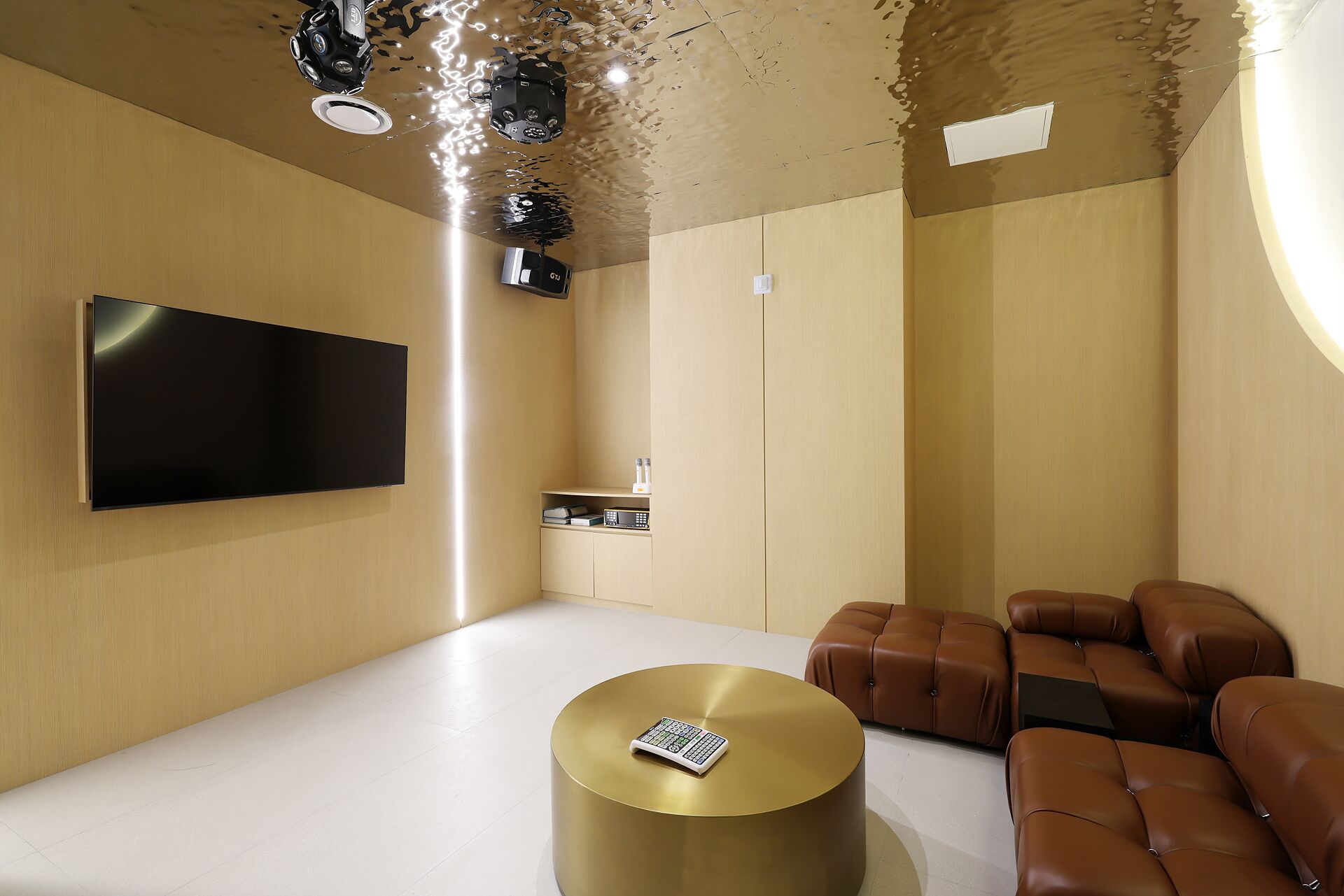 Una sala de estar moderna con un televisor de pantalla plana, una mesa de centro redonda dorada y sofás de cuero.