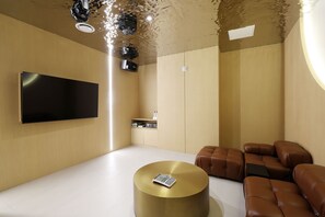 A modern living room with a flat-screen TV, a round gold coffee table, and leather sofas.