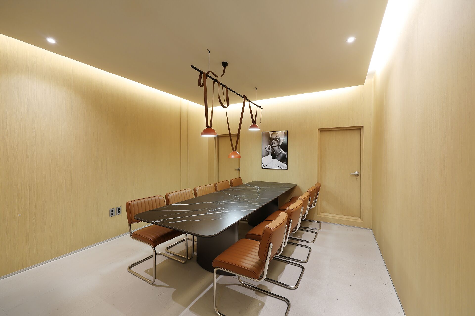 A conference room with a long table, multiple chairs, pendant lighting, and a door.
