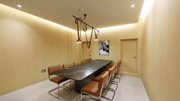 A conference room with a long table, multiple chairs, pendant lighting, and a door.