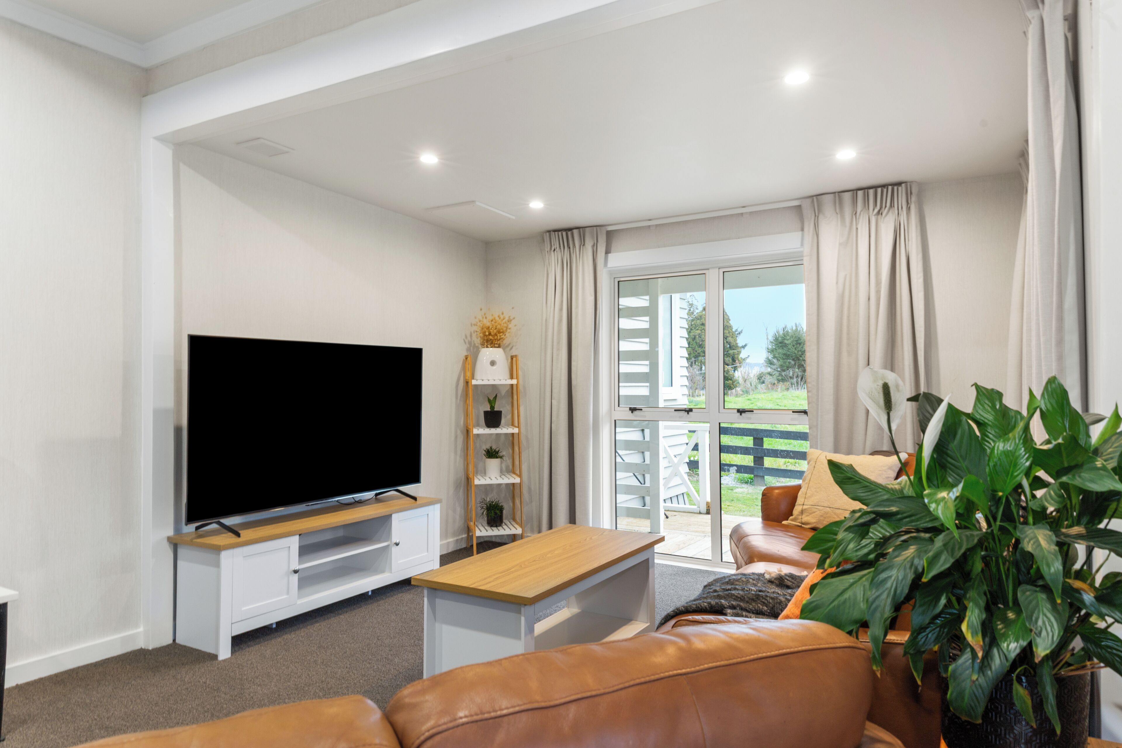 Una sala moderna con un televisor de pantalla plana, una mesa de centro de madera, un sofá de cuero y una planta grande en maceta.