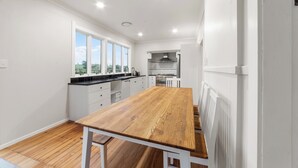A modern kitchen with white cabinets, a wooden table, and a view of the countryside through large windows.