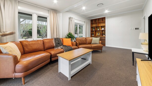 A spacious living room with a brown leather sofa, a wooden coffee table, and a bookshelf.
