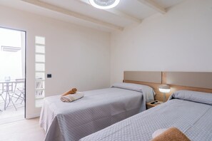 A hotel room with two beds, a small table, a chair, and a window.
